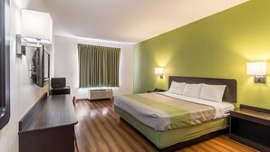 Hotelkamer met een bed, nachtkastjes, een bureau met stoel, een flatscreen-tv aan de muur, een raam met gordijnen en een muurlamp.