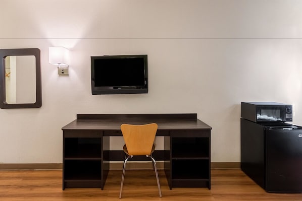 Quarto com escrivaninha de madeira escura, uma cadeira, TV de tela plana na parede e refrigerador preto.