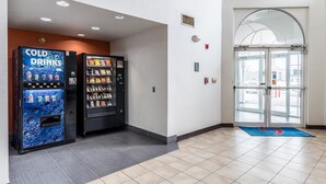 Een hotel lobby met automaten waarop 'COLD DRINKS' staat en een glazen entree.