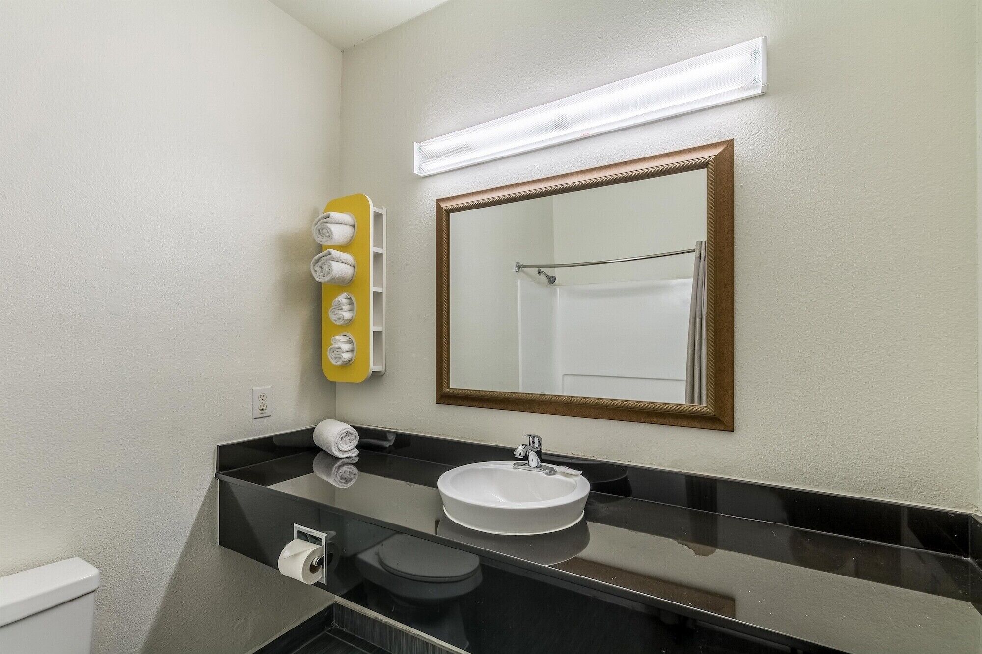 Un baño con lavamanos, espejo, toallero y retrete.