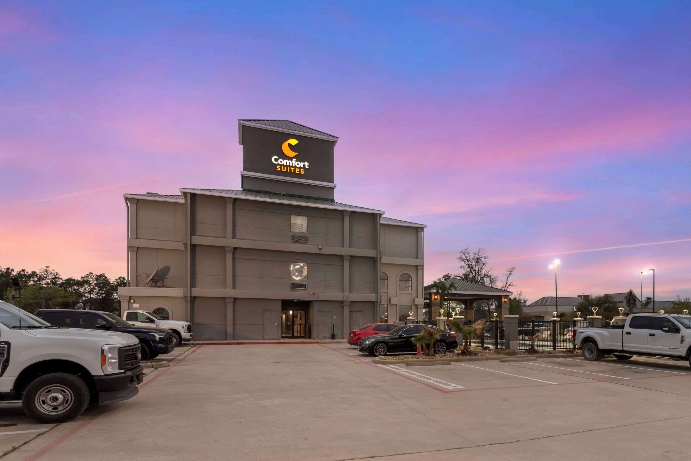 A hotel with a large sign reading "Comfort Suites" and a parking lot with several vehicles.