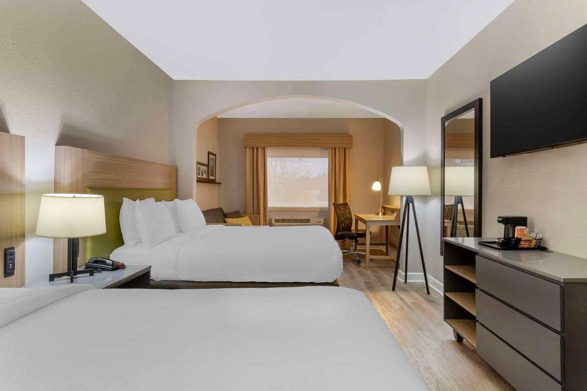 Une chambre d’hôtel avec deux lits, un bureau, une chaise, une télévision et une commode.