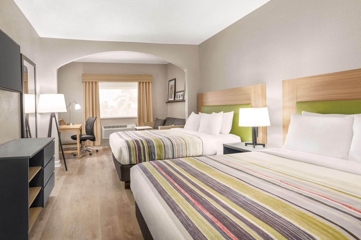 Une chambre d’hôtel avec deux lits, un bureau, une chaise, une lampe et une fenêtre avec des rideaux.