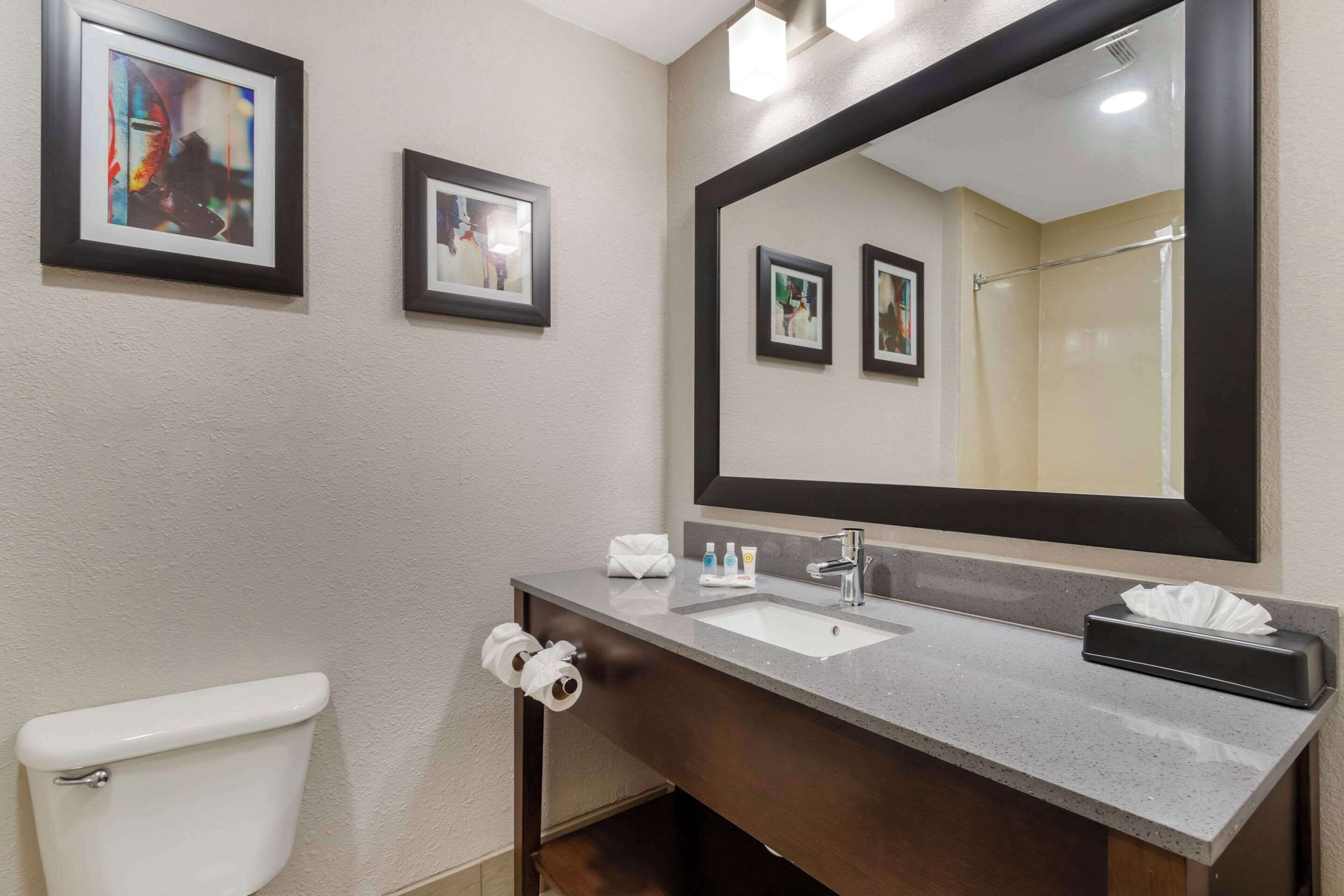 Un baño con un inodoro blanco, un lavamanos con espejo y cuadros en la pared.