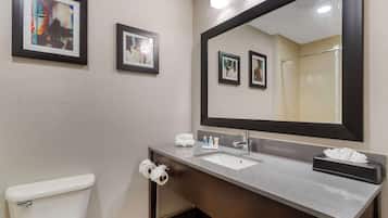 Un baño con un inodoro blanco, un lavamanos con espejo y cuadros en la pared.