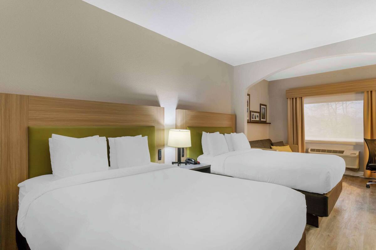 Une chambre d’hôtel avec deux lits, une table de chevet avec une lampe, une fenêtre avec des rideaux et un climatiseur fixé au mur.