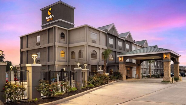 Un hotel con un llamativo letrero de 'Comfort Suites', una entrada cubierta y un jardín ajardinado con una fuente.