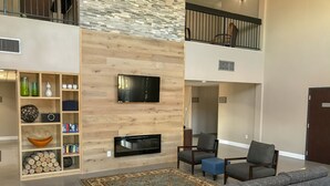 Una sala moderna con un sofá gris, un televisor de pantalla plana montado en una pared de madera, una chimenea y una estantería con objetos decorativos.