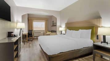 A hotel room with a large bed, a desk, a chair, and a window with curtains.