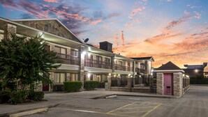 Un hotel de varios pisos con fachada de piedra, una zona exterior cubierta y un estacionamiento.