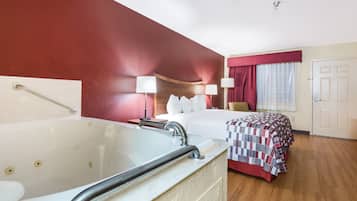 A hotel room with a large bathtub, a bed with a red and white checkered bedspread, two bedside lamps, and a wooden headboard.