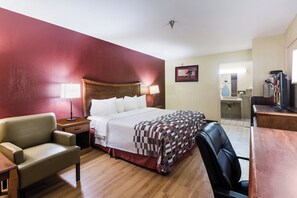A hotel room with a bed, a desk, a chair, a mirror, and a television. - Red Roof Inn Conroe North - Willis (Willis)