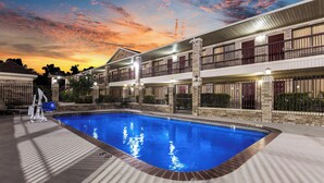 A swimming pool with a stone border, surrounded by a building with multiple balconies and a brick facade. - Red Roof Inn Conroe North - Willis (Willis)