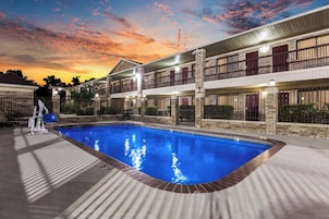 Una piscina con borde de piedra, rodeada por un edificio con múltiples balcones y fachada de ladrillo.