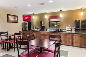 A dining area with a table and chairs, a kitchen counter with appliances, and a sign indicating free Wi-Fi availability. - Red Roof Inn Conroe North - Willis (Willis)