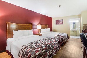 A hotel room with two beds, a wooden headboard, a red wall, a mirror, and a bathroom visible through an open door. - Red Roof Inn Conroe North - Willis (Willis)