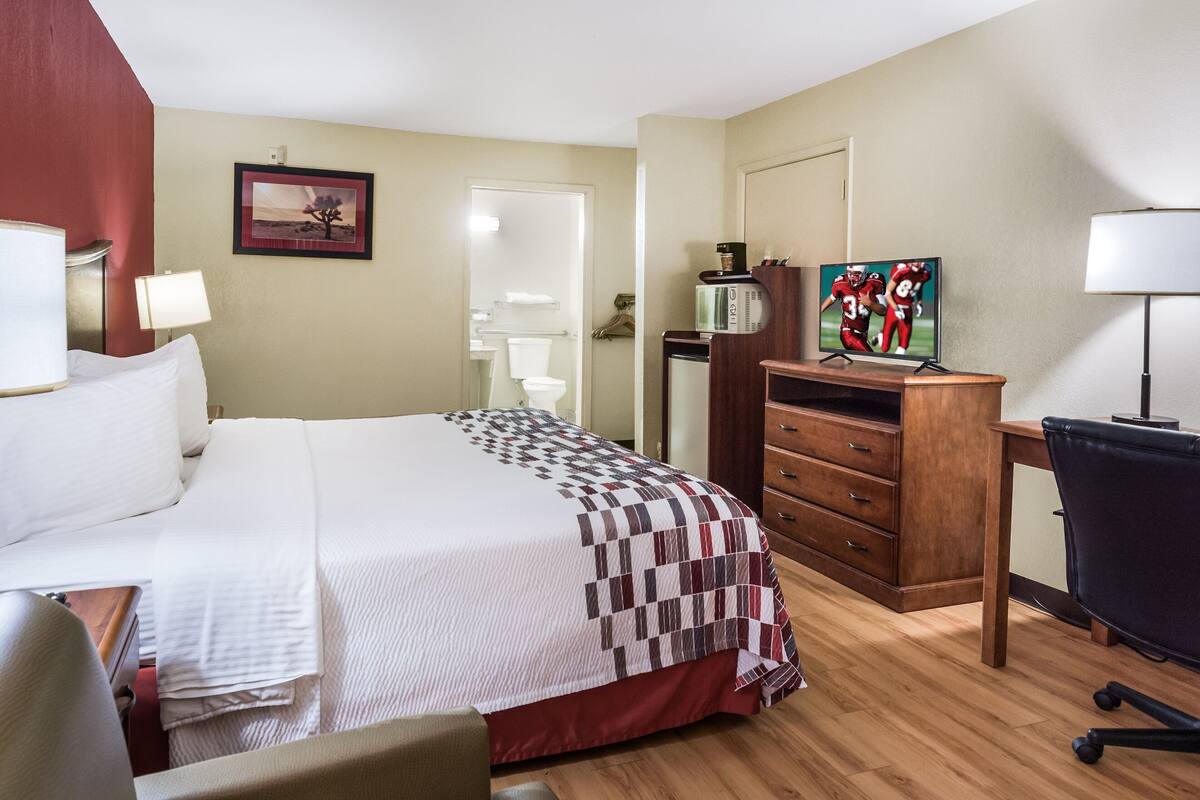 A hotel room with a bed, a desk, a chair, a TV, and a dresser.