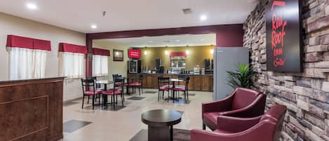 Un vestíbulo de hotel con una recepción, una zona de estar y una kitchenette al fondo.