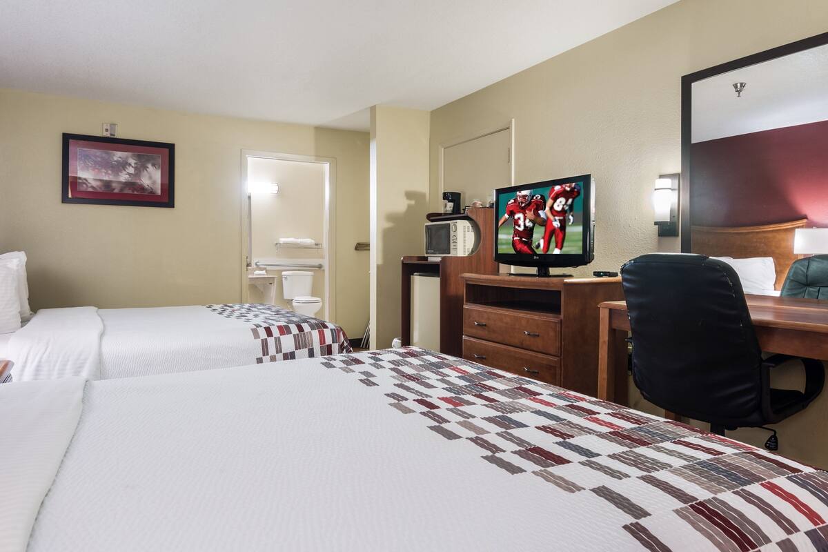 A hotel room with two beds, a desk with a computer, a TV, and a mirror.