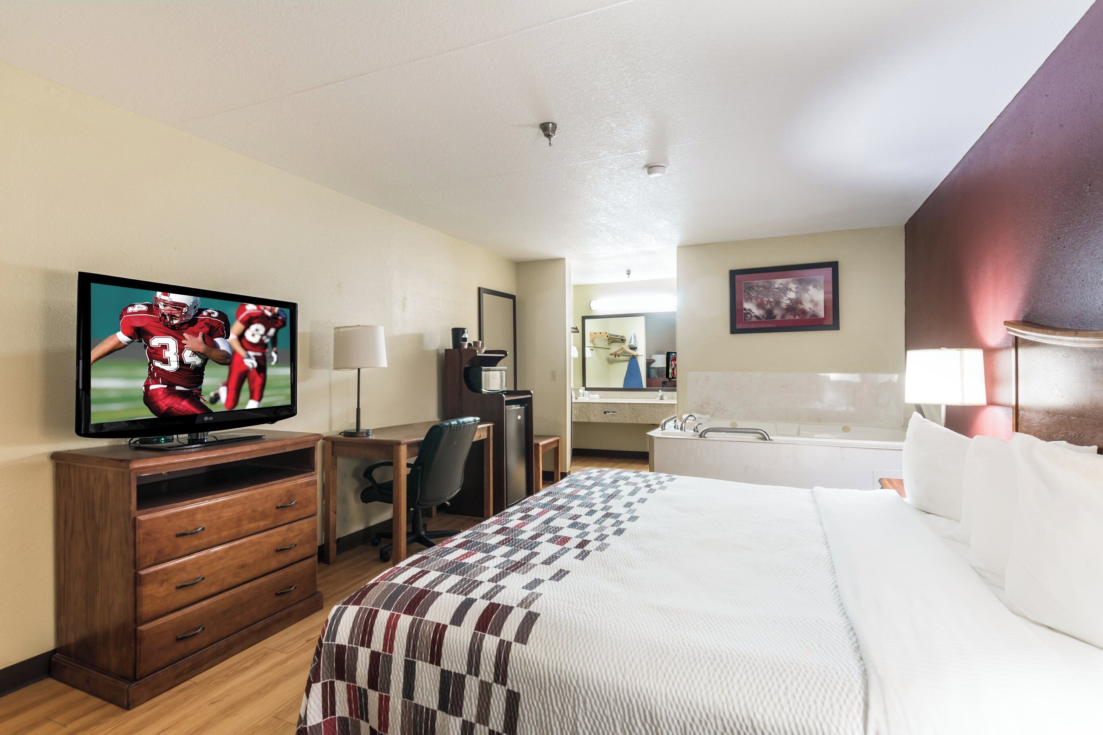 Ett hotellrum med en säng, ett skrivbord, en tv, en byrå, en spegel och ett badrum.