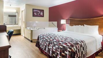 A hotel room with a bed, a desk, a chair, a bathroom, and a mirror.
