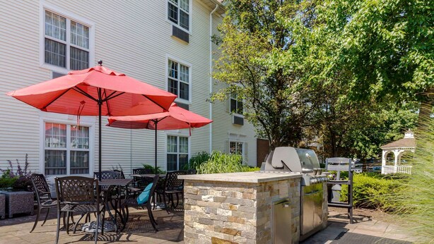 An outdoor patio with stone-tiled flooring, a barbecue grill, and a seating area with metal chairs and a red umbrella. - Extended Stay America Suites Chantilly Dulles (Chantilly)