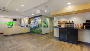 A hotel reception area with a wooden floor, a reception desk, a wall mural of a waterfall, and a counter with various amenities. - Extended Stay America Suites Chantilly Dulles (Chantilly)