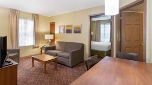 A hotel room with a sofa, a coffee table, a TV, a desk, and a dining table. - Extended Stay America Suites Chantilly Dulles (Chantilly)