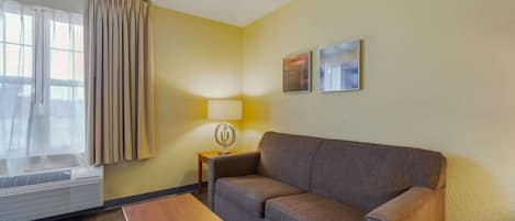 A hotel room with a sofa, a small table, a lamp, and two paintings on the wall.