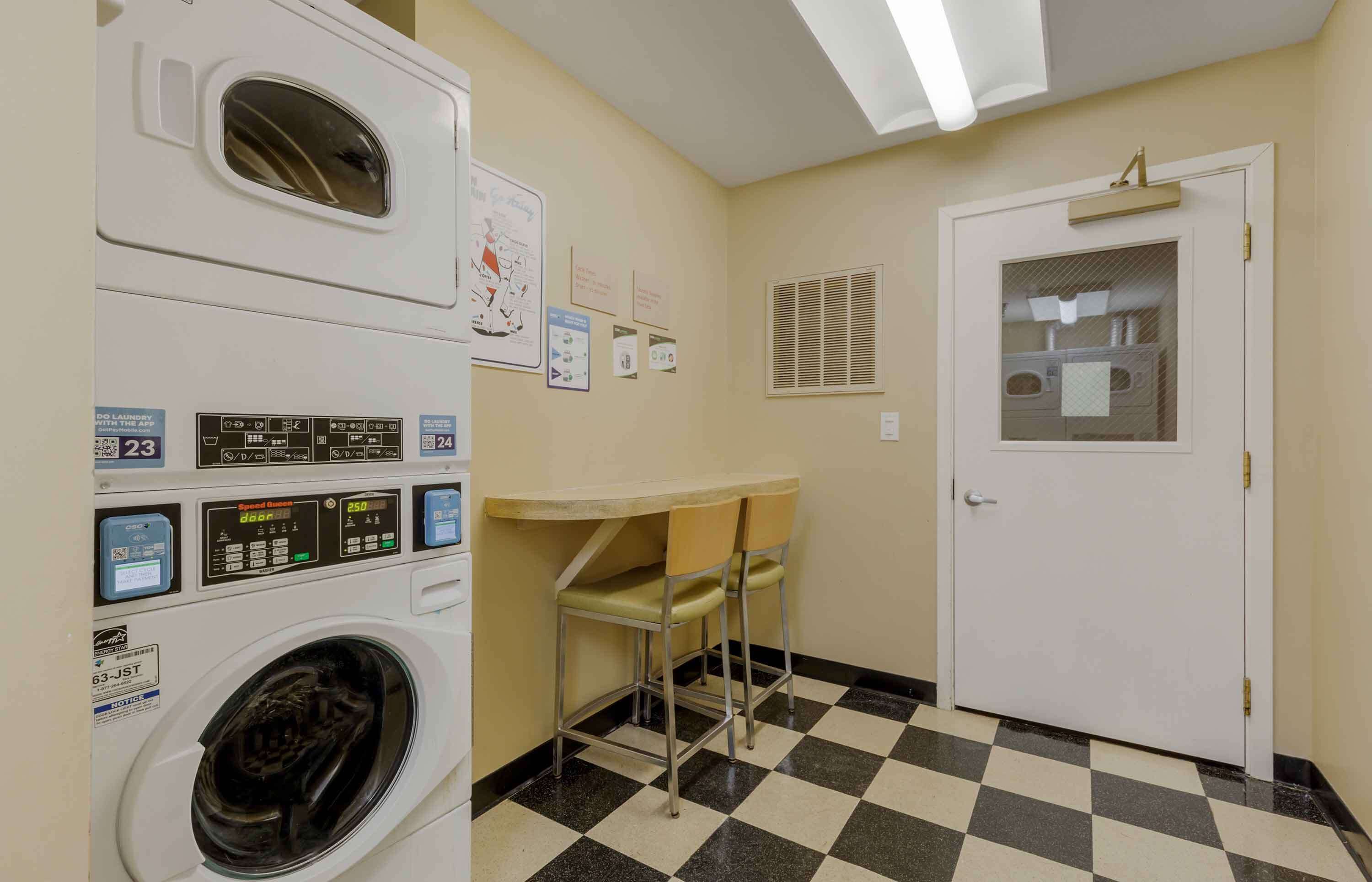 A laundry area with a washing machine, dryer, and a small table with chairs. There are signs on the wall and a door with a window.