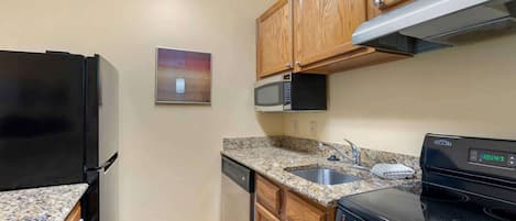 A kitchen with a black refrigerator, a microwave, a dishwasher, a granite countertop, a stainless steel sink, wooden cabinets, and a black stove.