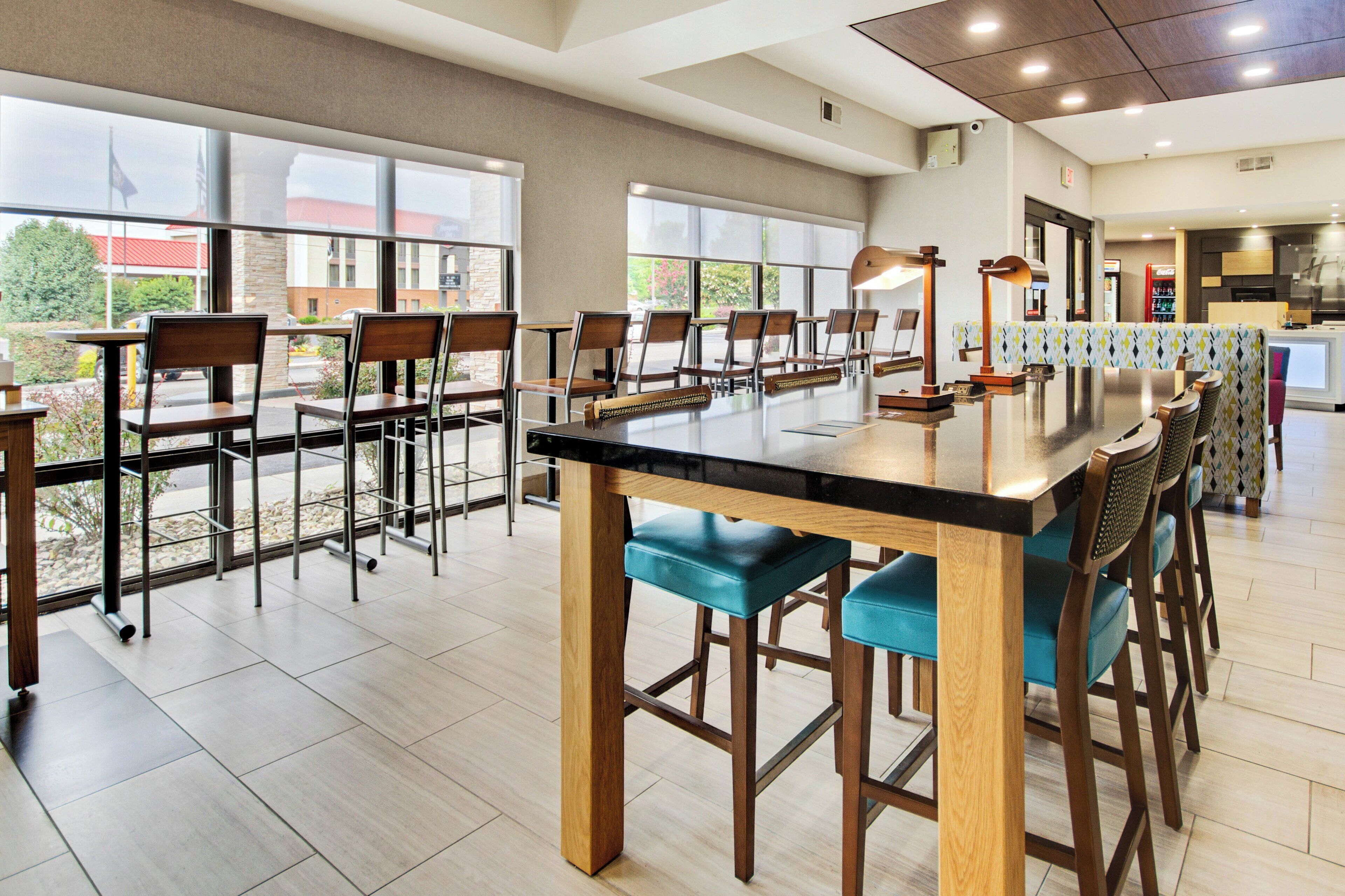 A modern dining area with a long communal table, bar stools, and a view of the outside.