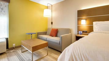 A hotel room with a sofa, a small table, a bed, a nightstand, and a wall-mounted lamp.