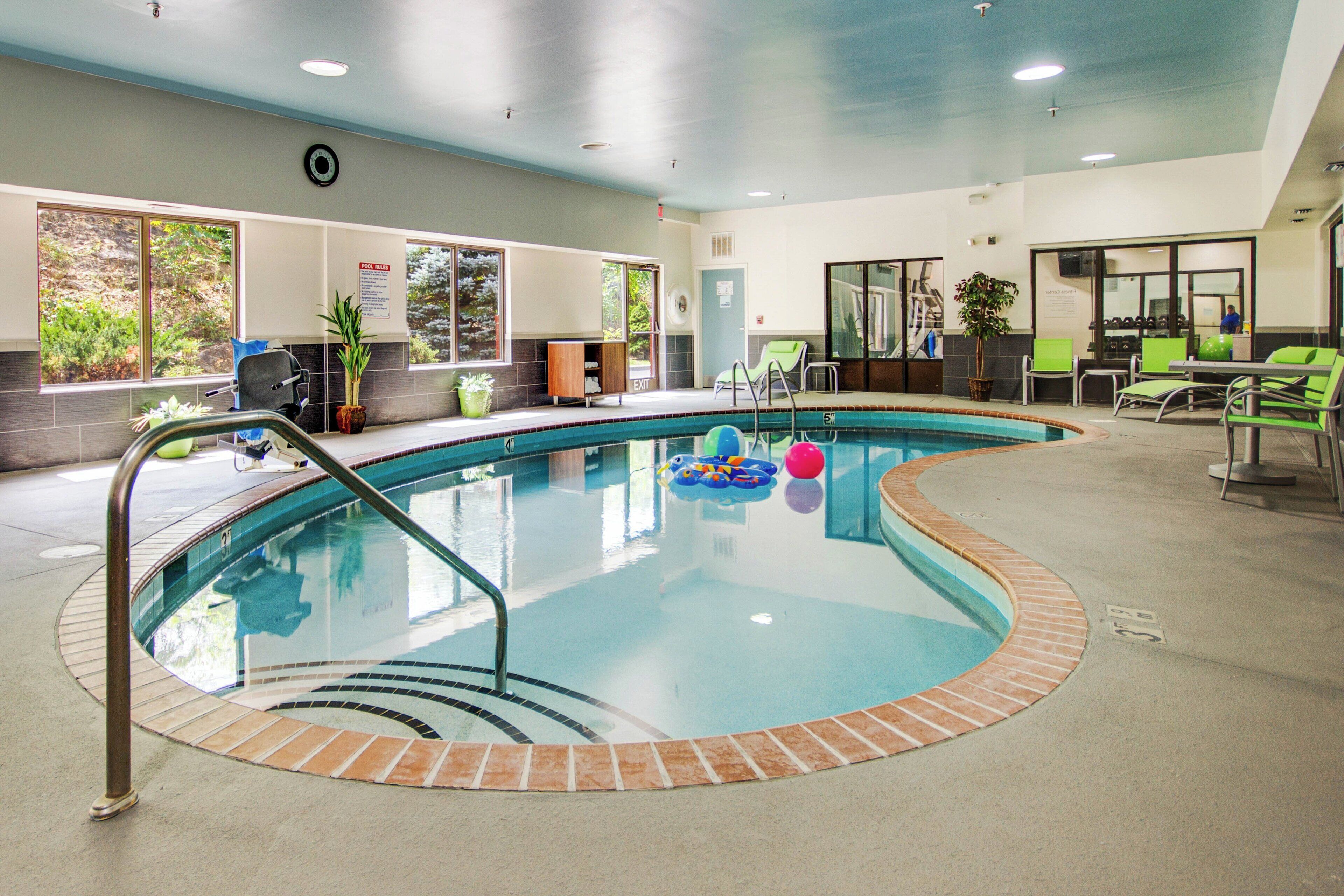 Piscina interna com superfície de água límpida, rodeada por um deck revestido de azulejos e uma borda de tijolos.