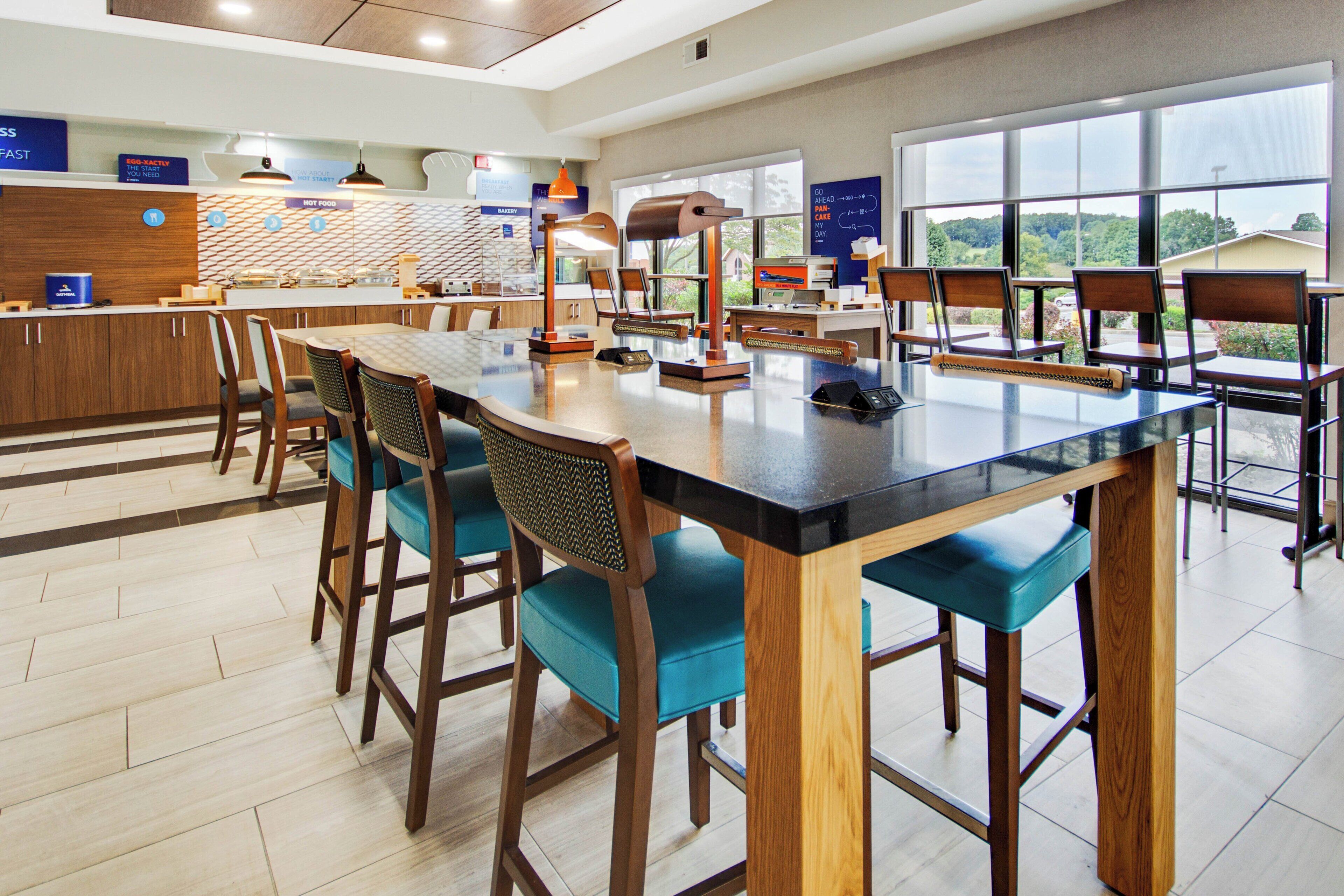 Un espace repas moderne avec une longue table, des tabourets de bar et un comptoir où sont présentés des plats.