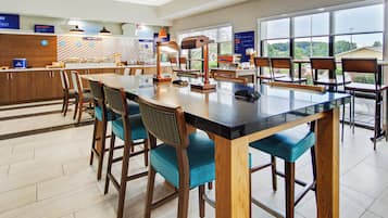Un espace repas moderne avec une longue table, des tabourets de bar et un comptoir où sont présentés des plats.