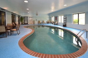 Una piscina interior con borde de ladrillo, rodeada de sillones de descanso y una mesa.