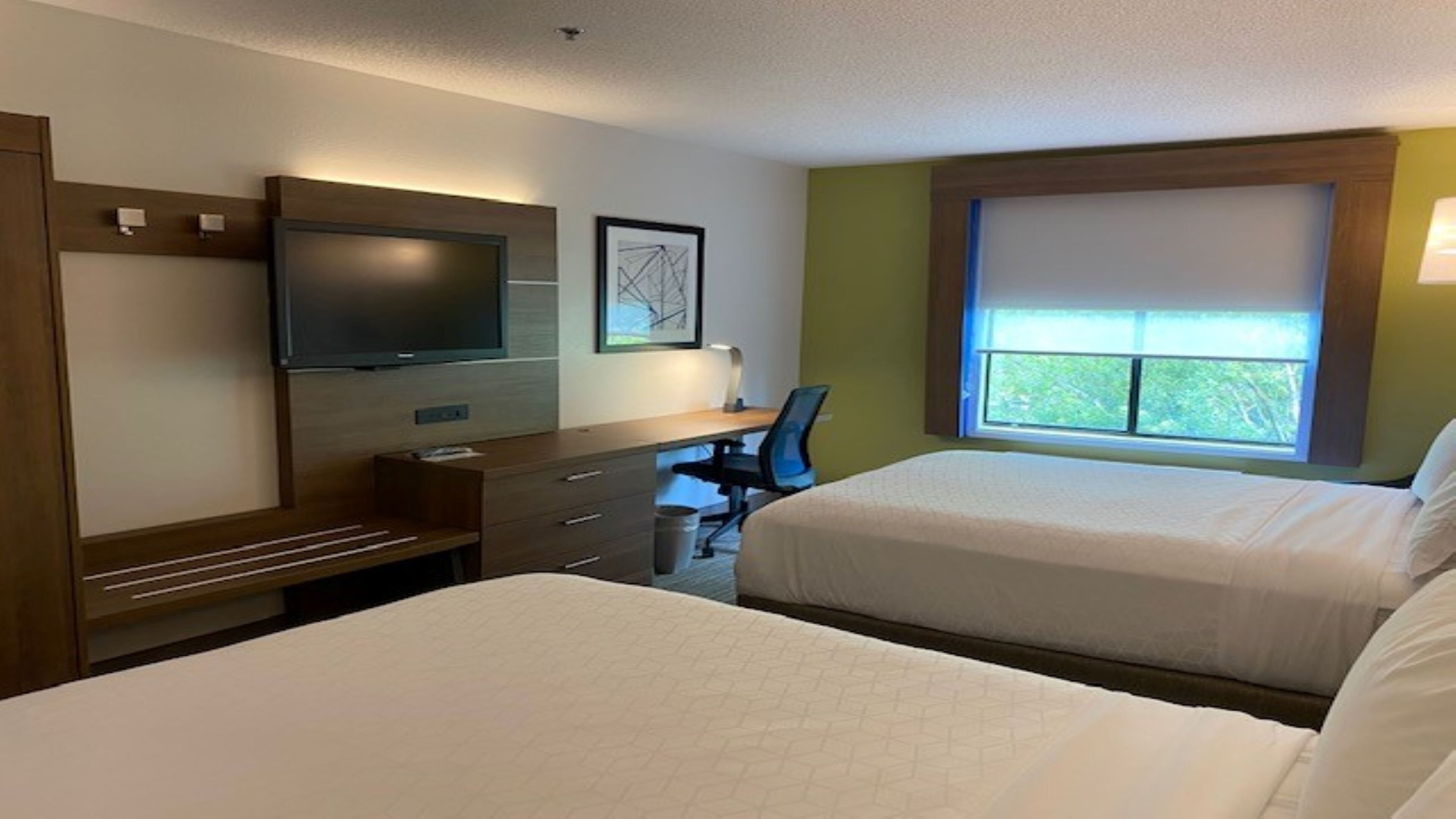 A hotel room with two beds, a desk, a chair, a television, and a window with a view.