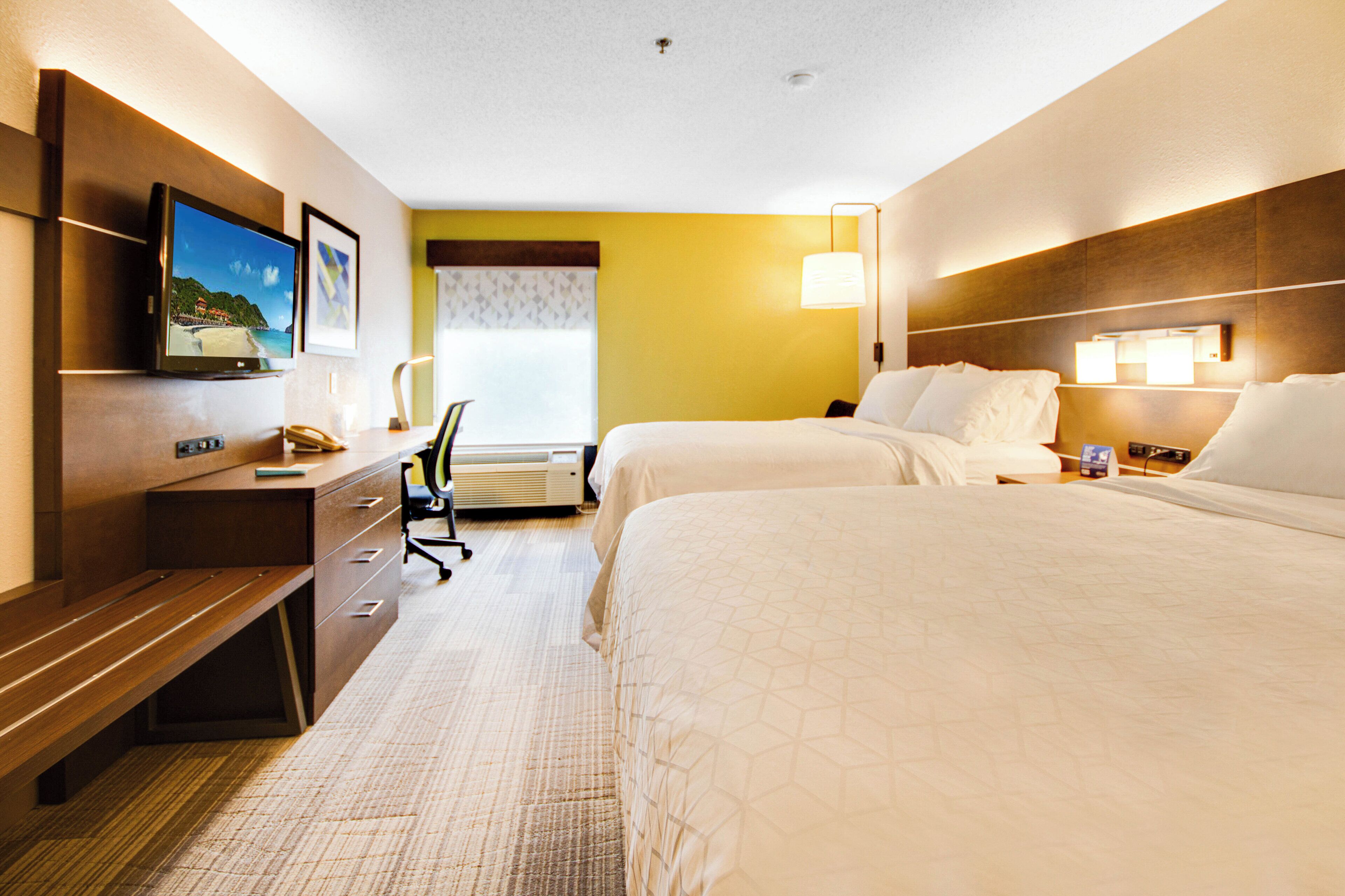 A hotel room with two beds, a desk, a chair, a television, and a window with blinds.