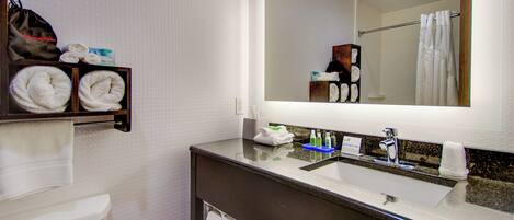 A hotel bathroom with a toilet, a sink, a mirror, and a towel rack with towels.