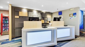 Zona d'entrada d'un hotel amb disseny modern, que inclou una recepció, una màquina de cafè i un frigorífic.
