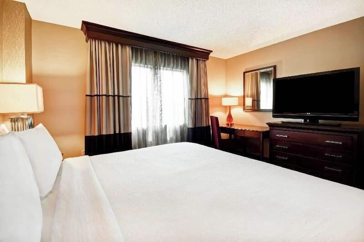 Une chambre d’hôtel avec un grand lit, un bureau avec une chaise, un téléviseur à écran plat et une fenêtre avec des rideaux.