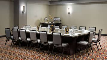 A conference room with a large rectangular table, grey upholstered chairs, and a patterned carpet.