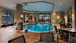 An indoor swimming pool with a view of the outside, surrounded by seating areas and a reception desk. - Embassy Suites by Hilton Dulles Airport (Herndon)