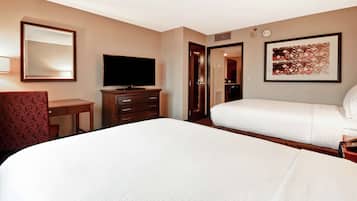 A hotel room with a large bed, a desk with a chair, a television, a wardrobe, and a bathroom door.