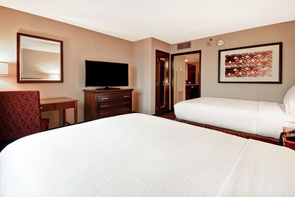 Habitación de hotel con una cama grande, un escritorio con silla, televisión, armario y la puerta del baño.