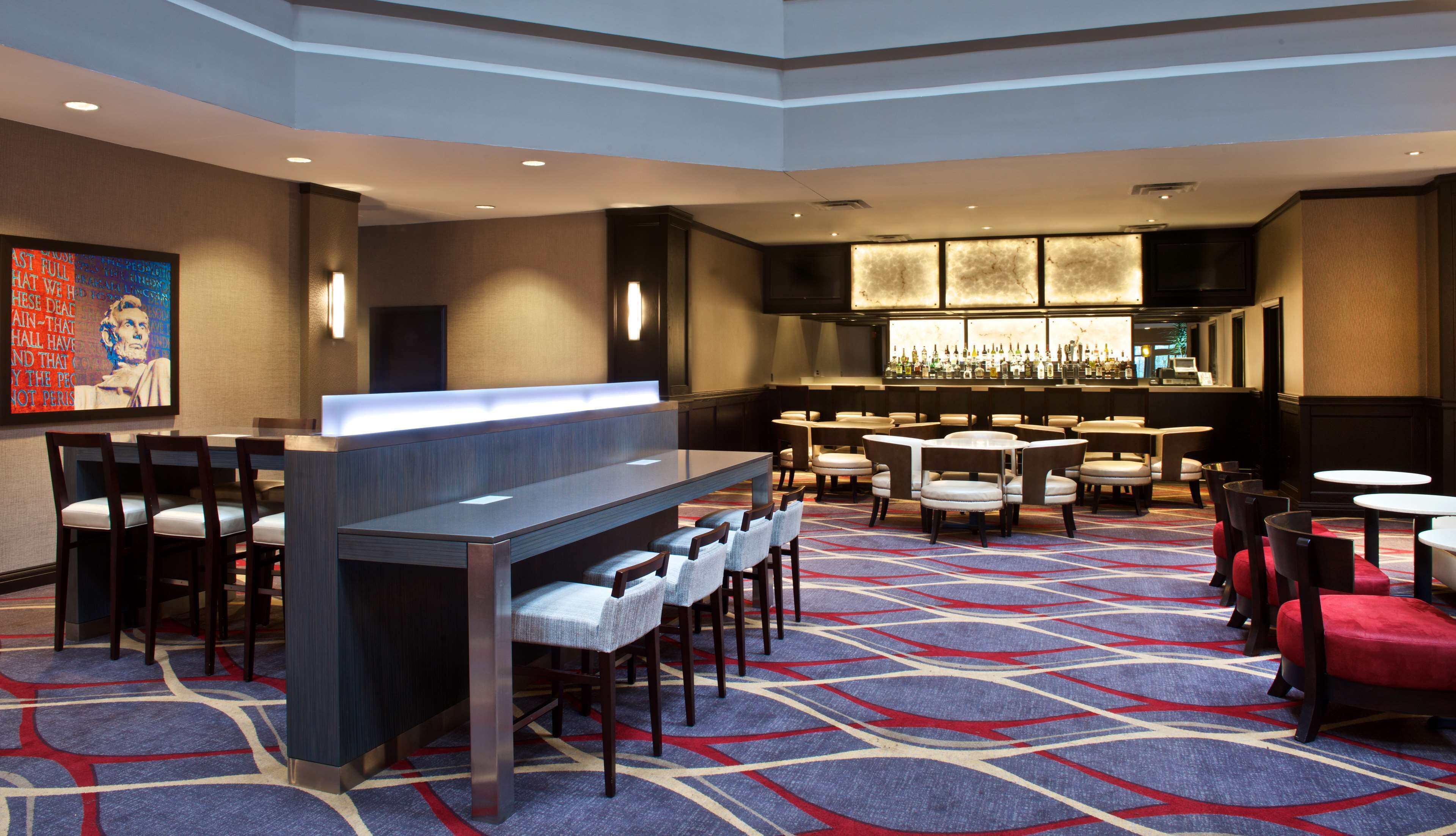 A hotel lobby with a bar area, multiple seating arrangements, and a patterned carpet.