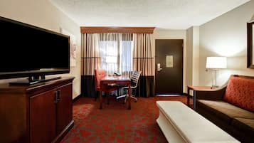 A hotel room with a flat-screen TV, a dining table with chairs, a sofa, a bench, and a lamp.