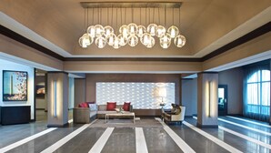 A spacious lobby with a modern chandelier, a seating area with sofas and armchairs, and a patterned wall. - Embassy Suites by Hilton Dulles Airport (Herndon)