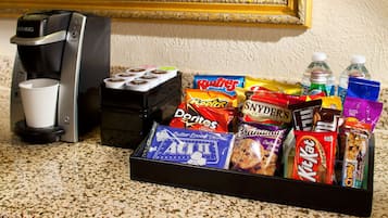 A coffee maker, a cup, and a snack tray with various items like chips, cookies, and drinks.